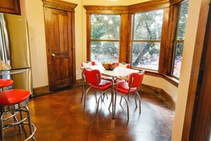 A kitchen with a dining table, chairs, a refrigerator, and a window with a view of trees.