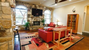 Una sala de estar con chimenea de piedra, sofá de cuero rojo y televisor montado en la pared.