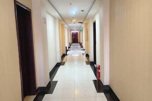 Corredor de hotel com padrão quadriculado no chão, portas em ambos os lados e um extintor de incêndio à direita.