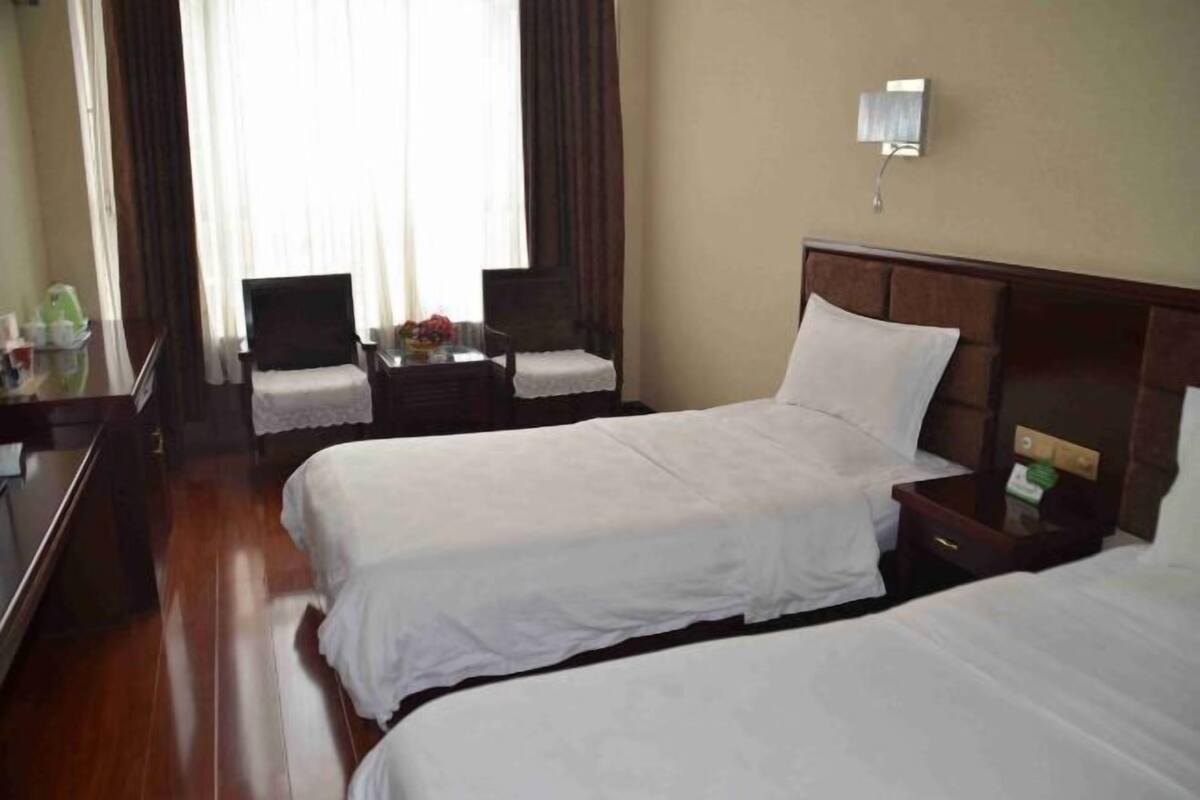 A hotel room with two beds, a desk, a chair, and a small table with a lamp.