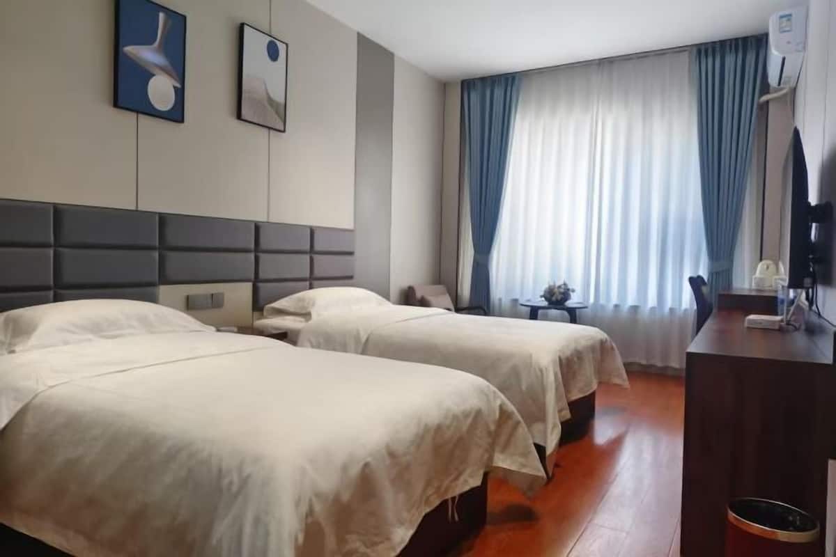 A hotel room with two beds, a desk, a chair, a TV, and a window with curtains.