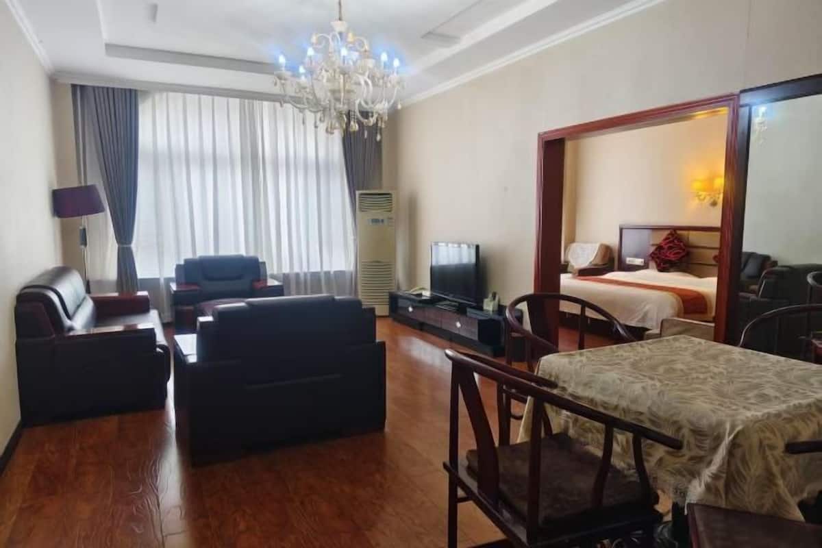 A hotel room with a sofa, a TV, a bed, a dining table, and a chandelier.