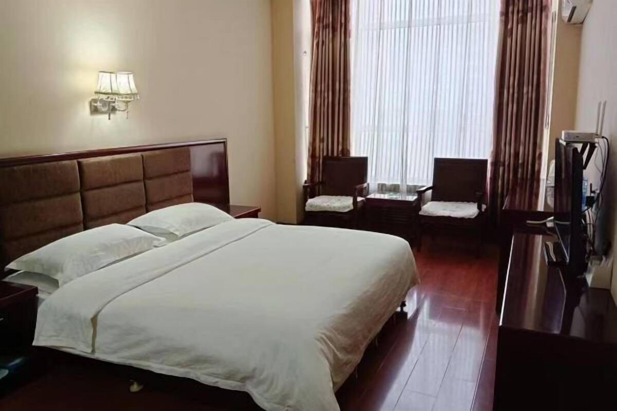 A hotel room with a large bed, two bedside tables, a desk with a chair, a TV, and a window with curtains.