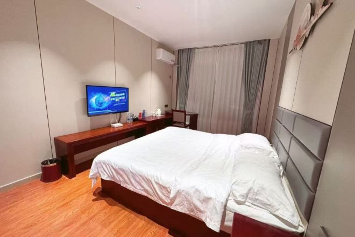 Una habitación de hotel con una cama, un televisor, un banco de madera y una cortina.