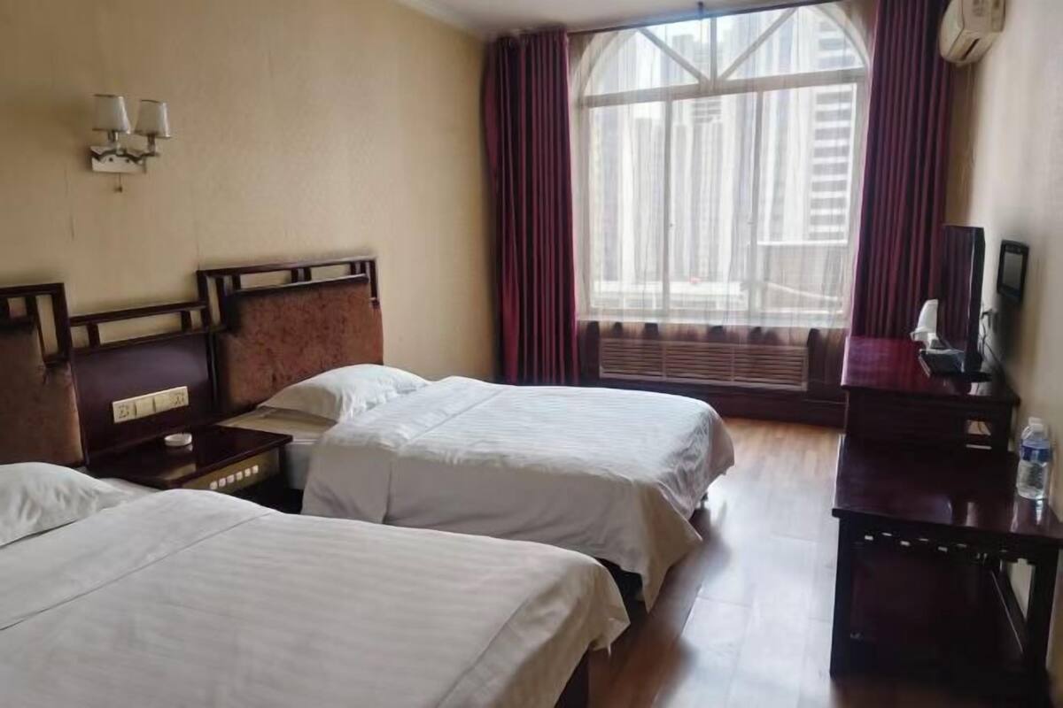 A hotel room with two beds, a nightstand, a desk, and a window with curtains.