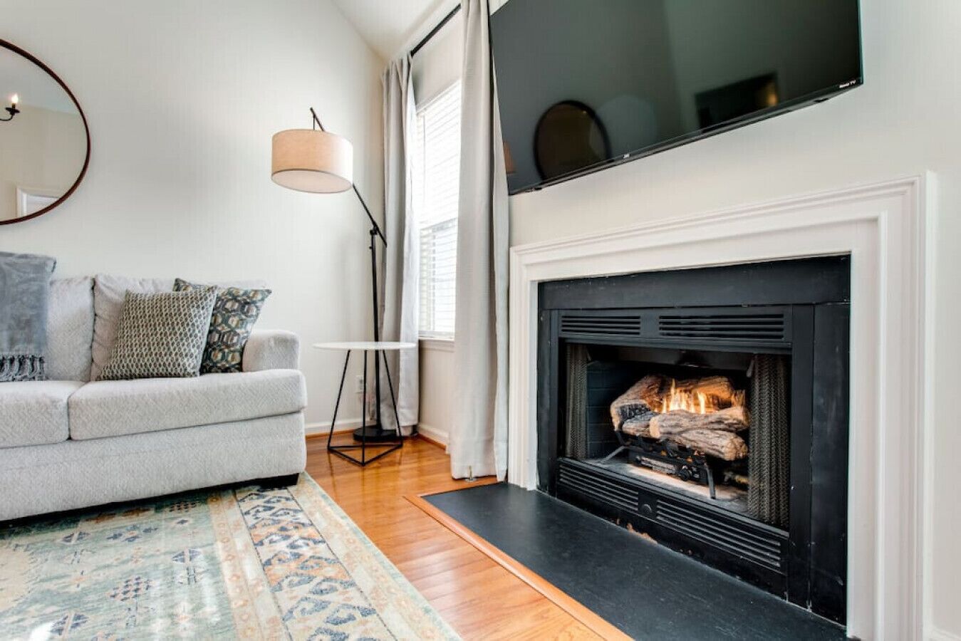 A living room with a fireplace, a grey sofa, a patterned rug, and a floor lamp.