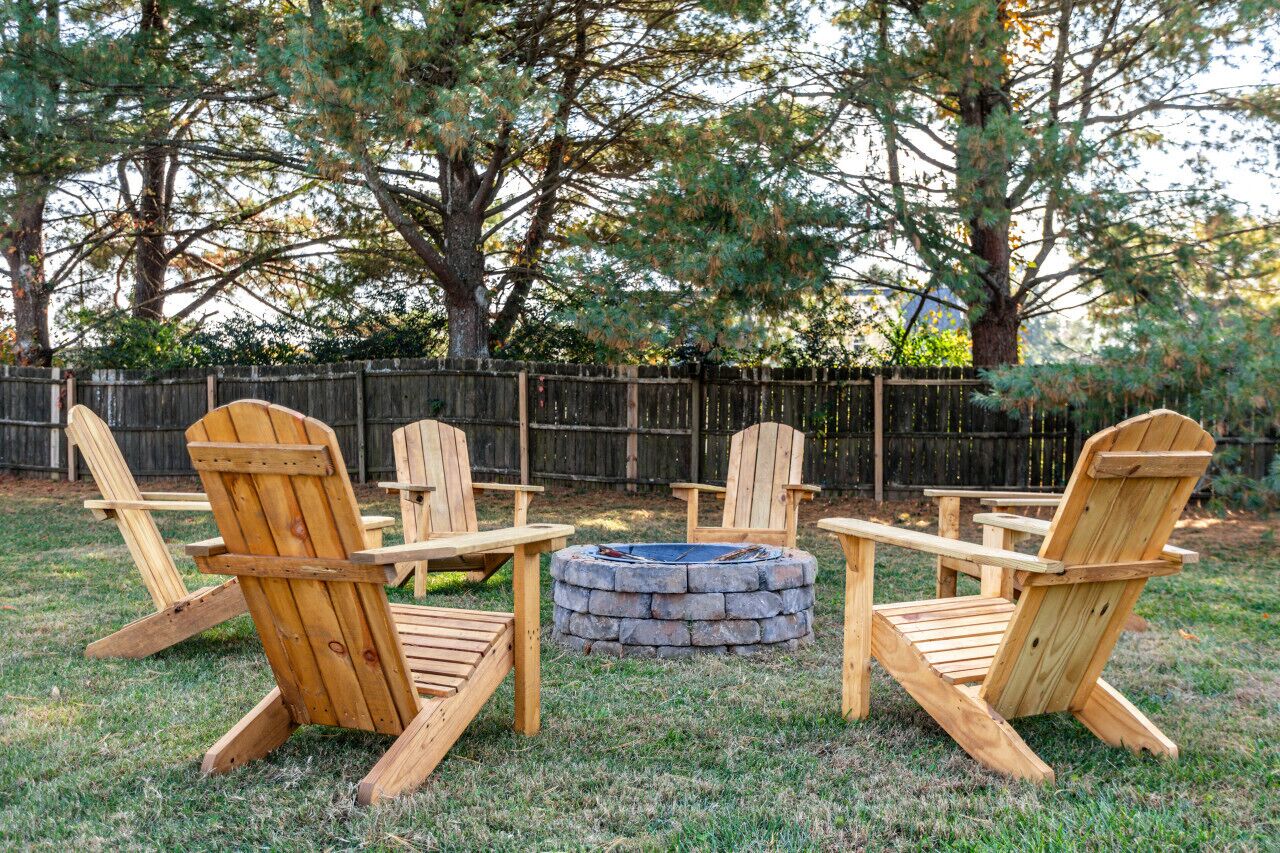 Un giardino con quattro poltrone Adirondack in legno disposte attorno a un braciere in pietra.