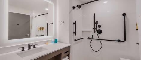 A modern bathroom with a large mirror, dual sinks, a shower with a black frame, and a small table.