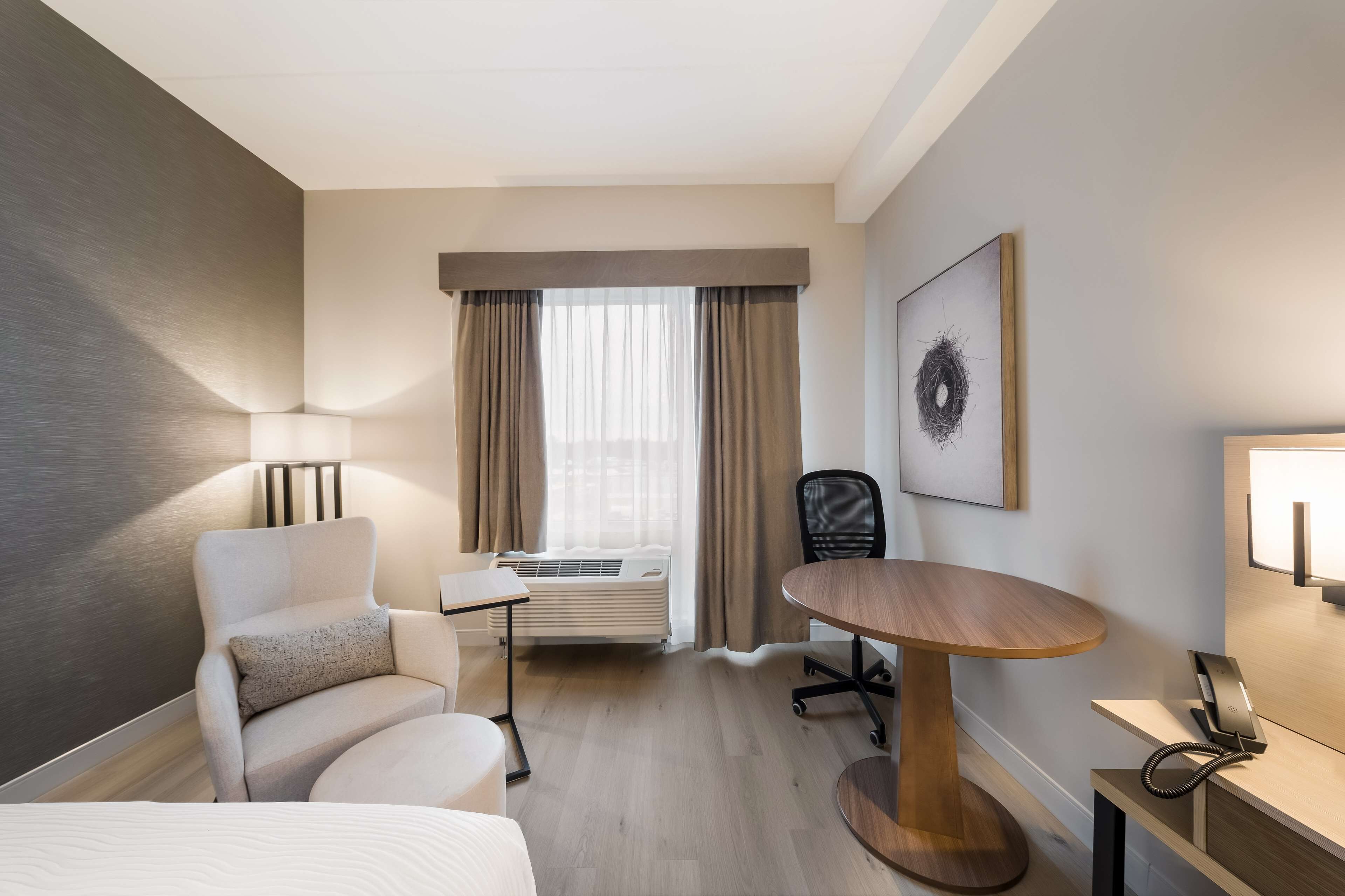 Une chambre d’hôtel équipée d’un lit, d’un bureau, d’une chaise, d’une lampe, d’un téléphone et d’une fenêtre avec des rideaux.