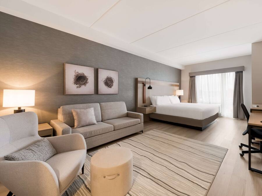 Een hotelkamer met een bank, een bed, een bureau en een klein voetenbankje. Er zijn twee wandlampen en een flatscreen televisie.