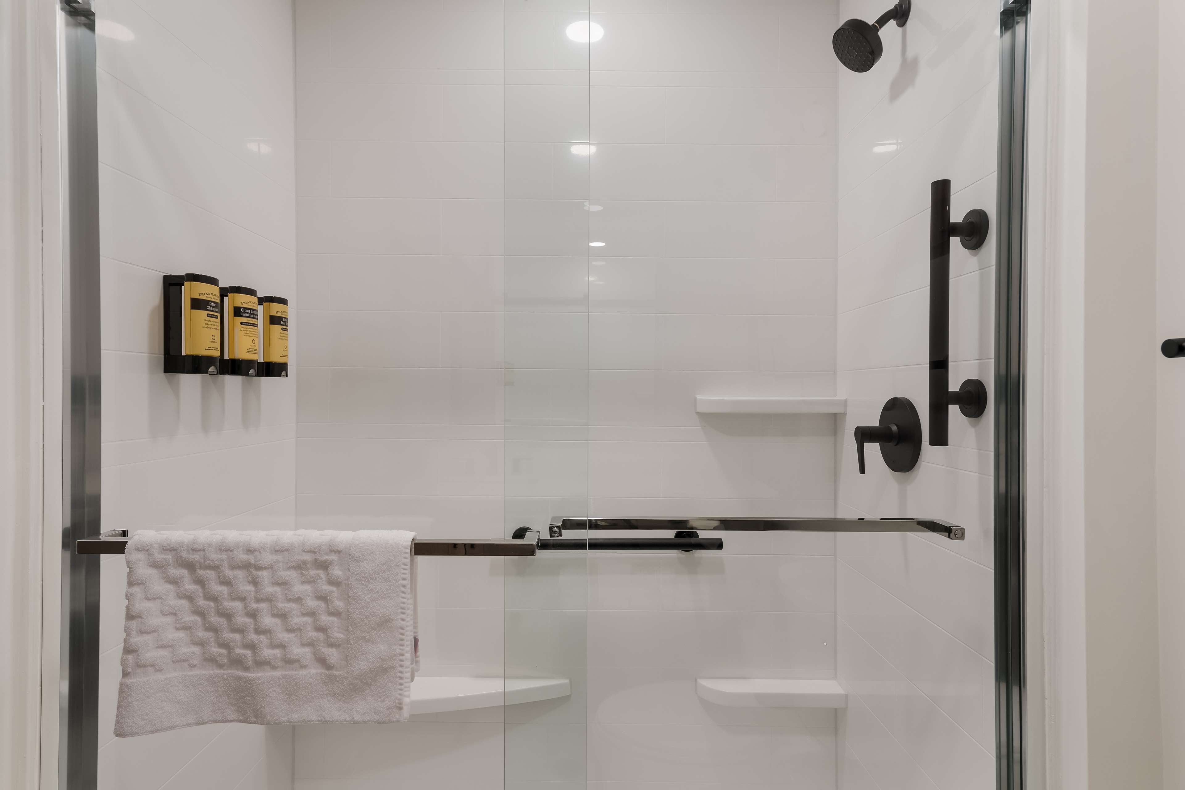 A glass-enclosed shower area with a towel rack, a glass door, and a shelf with toiletries.