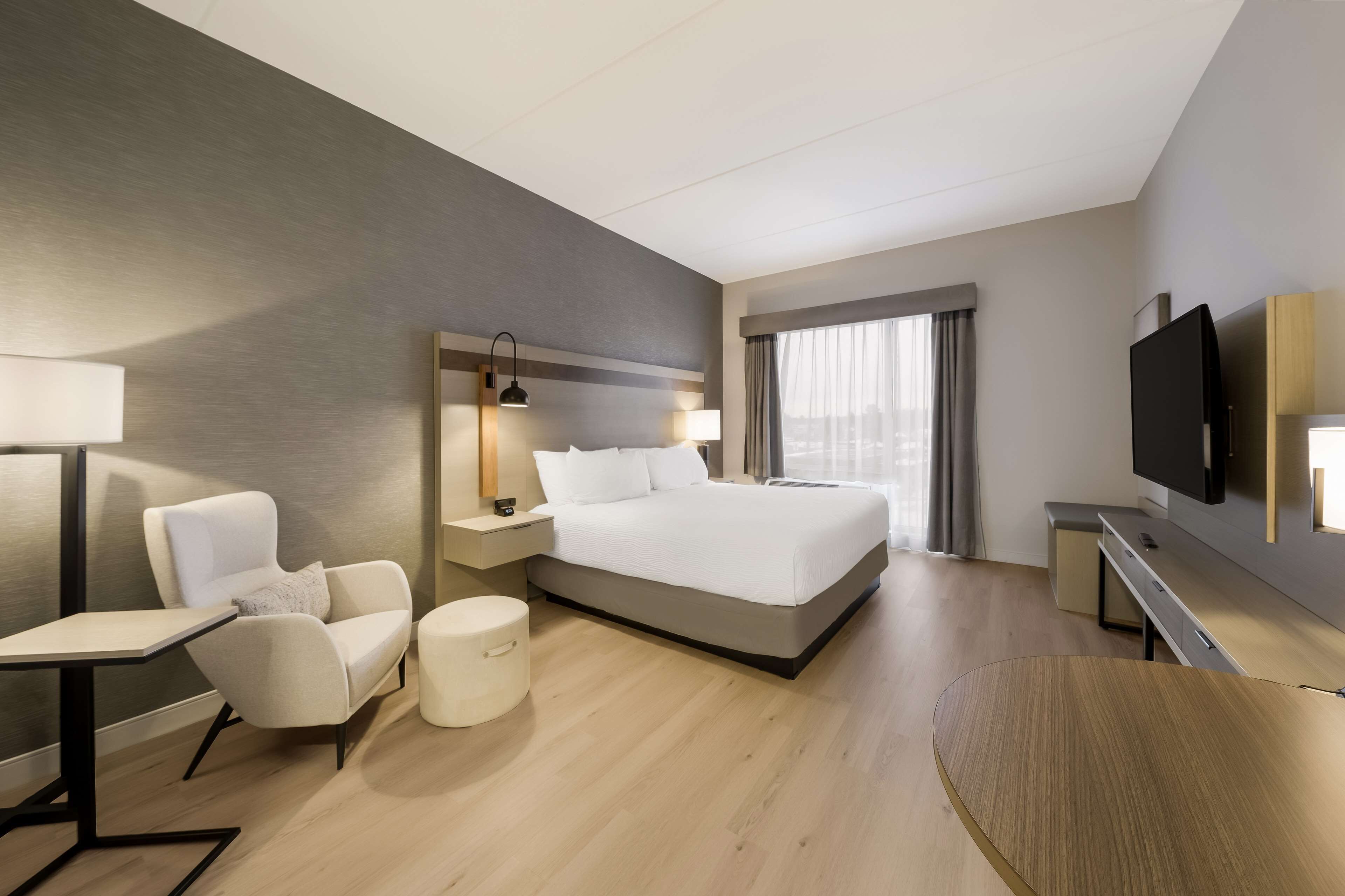 A modern hotel room with a large bed, a desk, a chair, a TV, and a window with curtains.