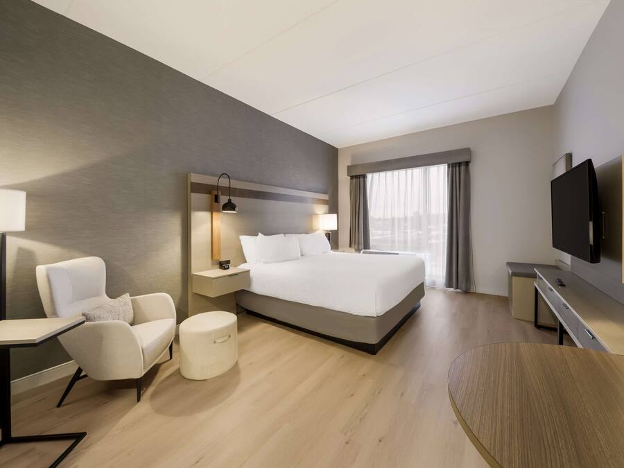 A modern hotel room with a large bed, a desk, a chair, a TV, and a window with curtains.