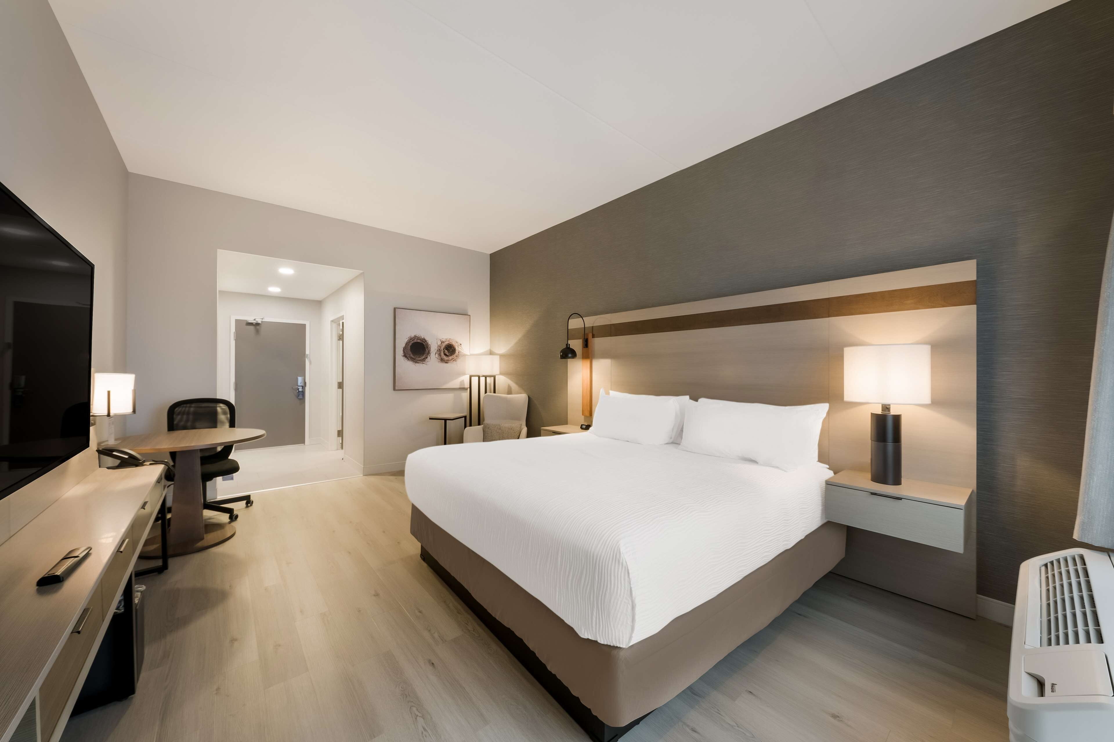 Una habitación de hotel con una cama grande, un escritorio con una silla, un televisor y una lámpara.