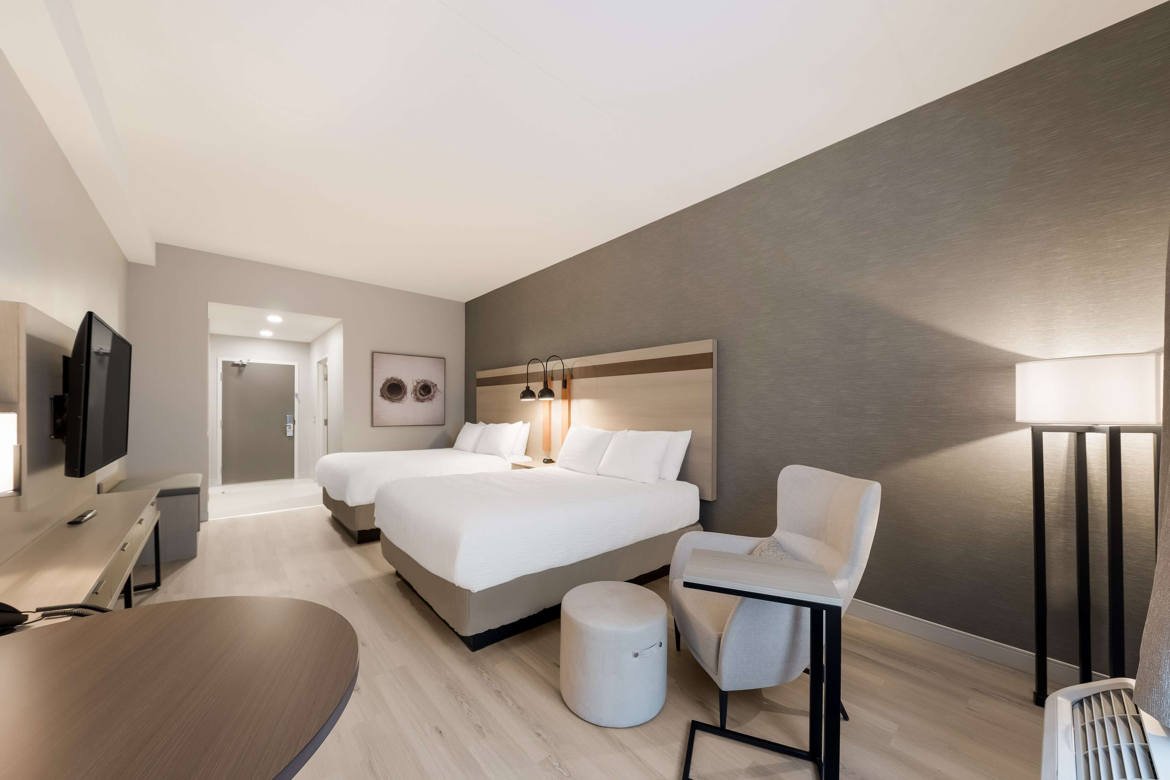 Ein modernes Hotelzimmer mit einem großen Bett, einem Schreibtisch, einem Sessel, einem Fernseher und einer Lampe.