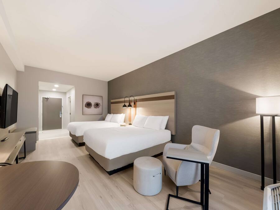 A modern hotel room with a large bed, a desk, a chair, a TV, and a lamp.