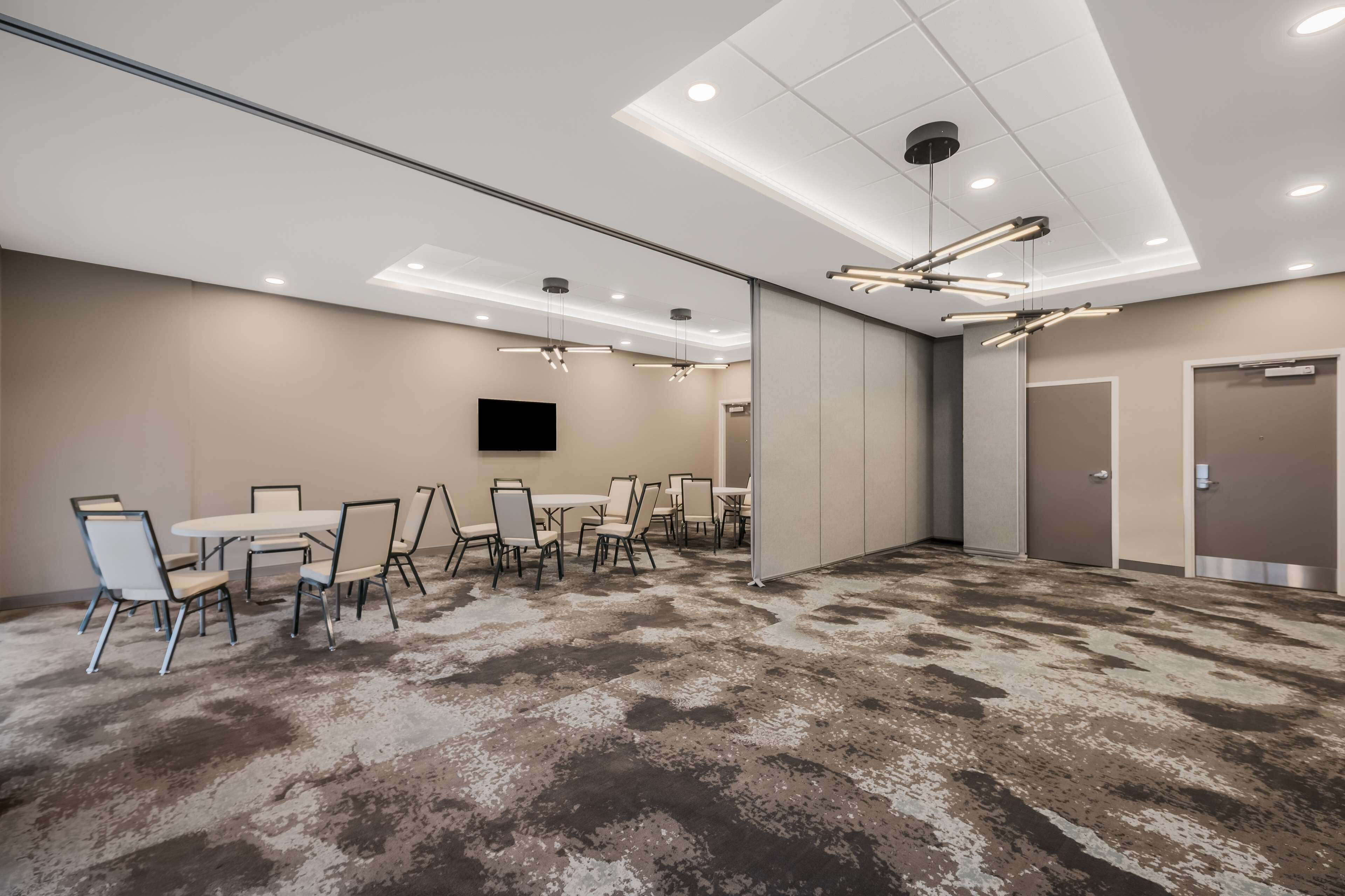 Une salle de conférence dotée d’un sol recouvert de moquette, de murs blancs et d’un téléviseur à écran plat fixé au mur.
