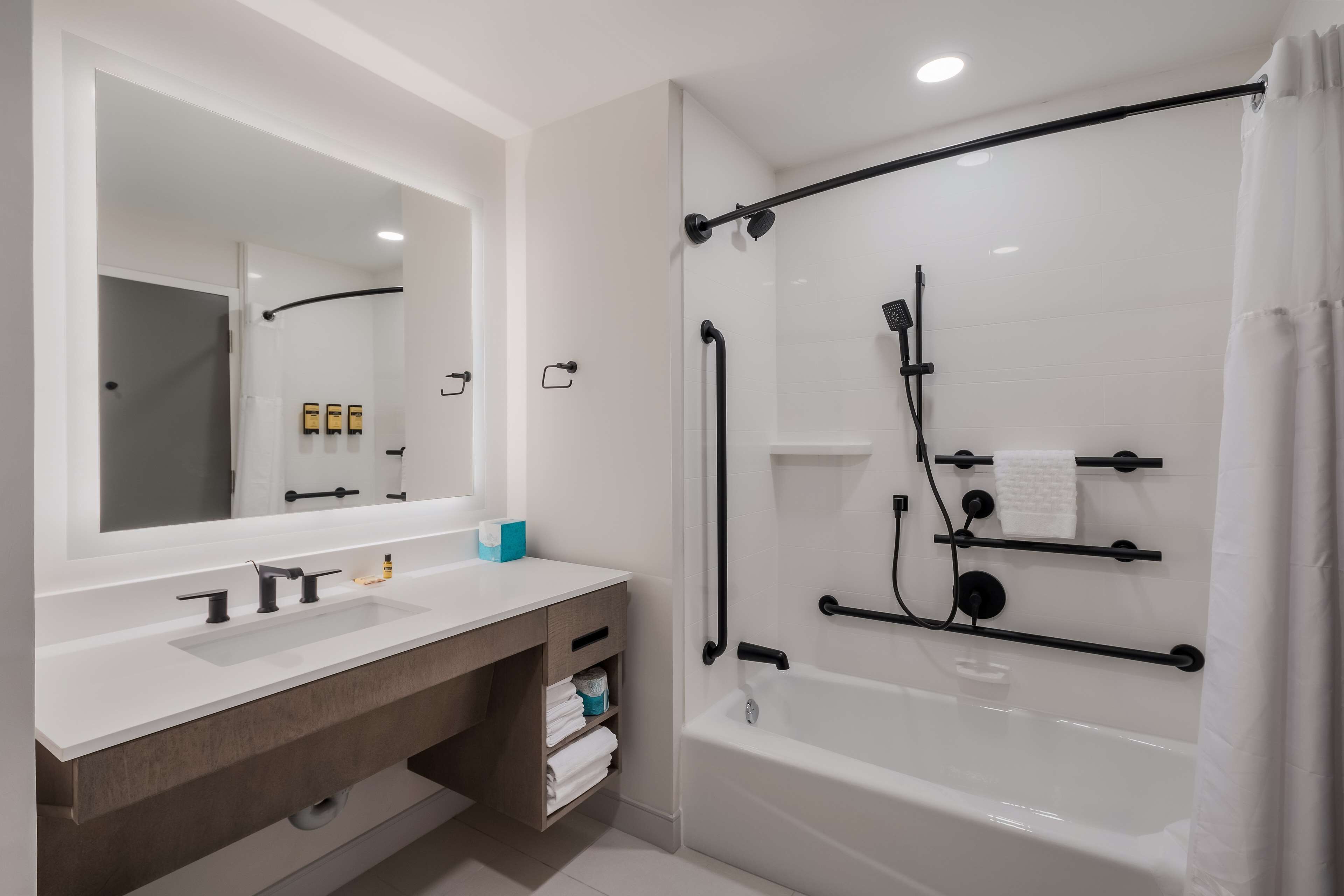 Un baño moderno con un tocador blanco, un espejo grande, una bañera y una zona de ducha con puerta de cristal.