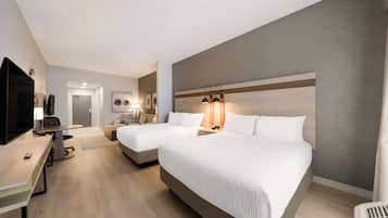 Una habitación de hotel con dos camas, un escritorio con televisor y una mesita pequeña.
