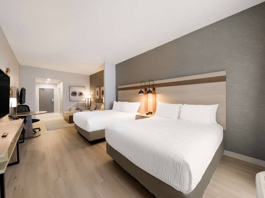 Una habitación de hotel con dos camas, un escritorio con televisor y una mesita pequeña.