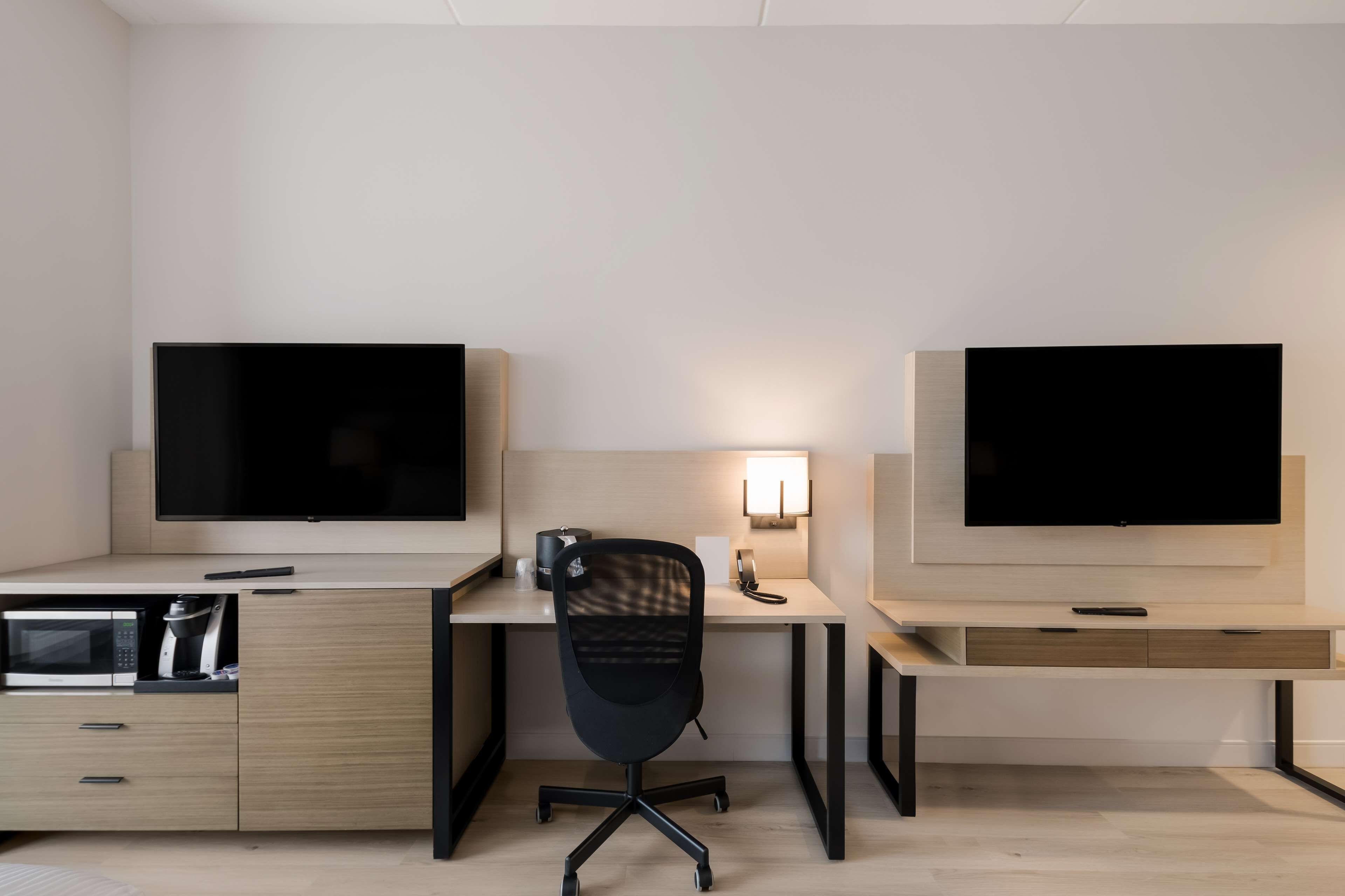 A modern office space with two desks, each with a flat-screen monitor, a chair, and a built-in coffee machine.