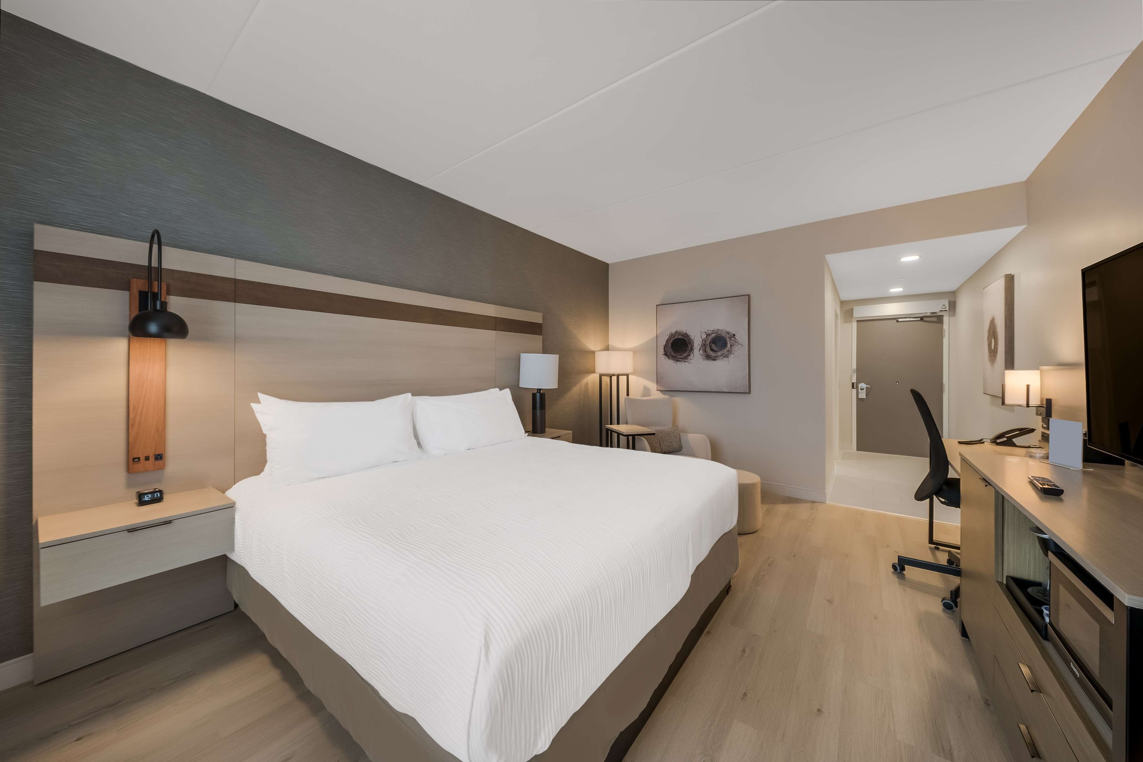 Habitación de hotel moderna con una cama grande, mesitas de noche, un escritorio con silla y un baño visible a través de una puerta abierta.