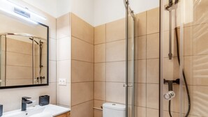 A modern bathroom with a glass-enclosed shower, a white toilet, and a sink with a towel. - Studio Aristide - Welkeys (Cabourg)