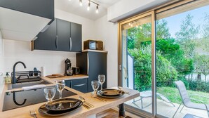 A modern kitchen with dark cabinets, a wooden countertop, and a dining area with a table set for two. - Studio Aristide - Welkeys (Cabourg)