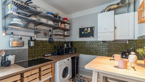 A compact kitchen with a washing machine, wooden cabinets, and a tiled backsplash. - Appartement de la Bannière - Welkeys (Lyon)