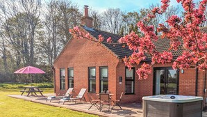 A brick house with a patio, a hot tub, and a picnic table with chairs. - Lie back and count the stars whilst lazing in the hot tub. (Gissing, near Diss)