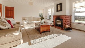 A living room with a fireplace, a sofa, a coffee table, and a large window. - Lie back and count the stars whilst lazing in the hot tub. (Gissing, near Diss)