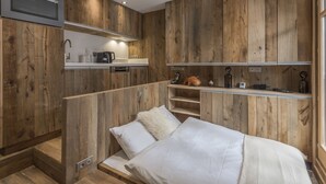 A compact bedroom with a bed, a built-in kitchenette, and wooden paneling.