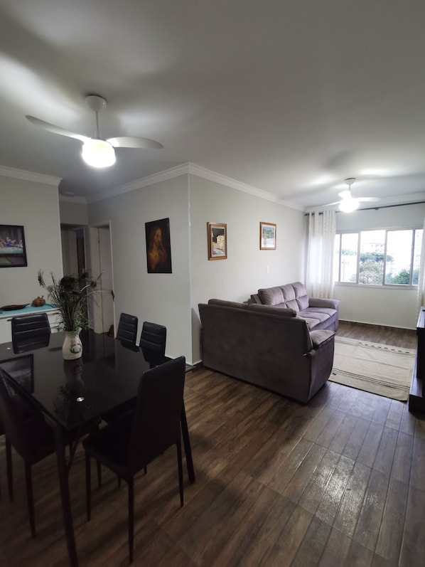 A modern living room with a dining area, wooden flooring, a gray sofa, and ceiling fans.