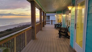 Une terrasse en bois offrant une vue sur la plage, des sièges d’extérieur et un bâtiment à la façade verdoyante.