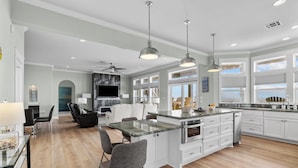 Une cuisine moderne avec des meubles blancs, un grand îlot central et des luminaires suspendus.
