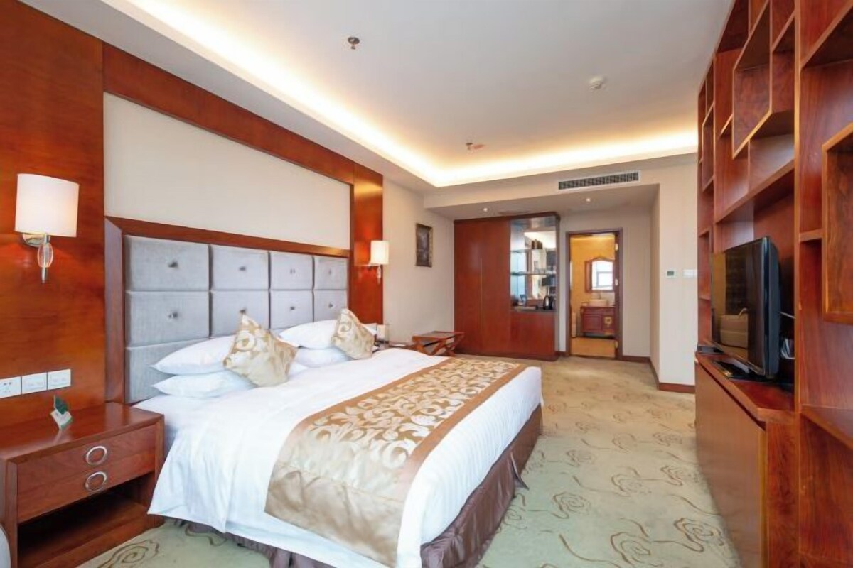 A hotel room with a large bed, bedside tables, a TV, and a mirror.