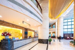 A hotel lobby with a reception desk, marble columns, and a spacious area with seating.