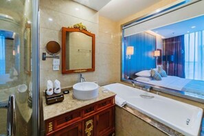 A modern bathroom with a large mirror, a round sink, a bathtub, and a view of a bedroom with a bed and curtains.