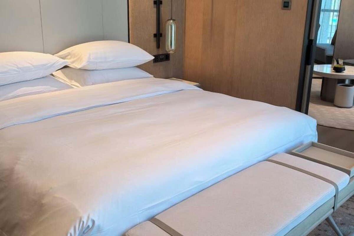 A bed with white linens, a bedside table, and a wooden headboard.