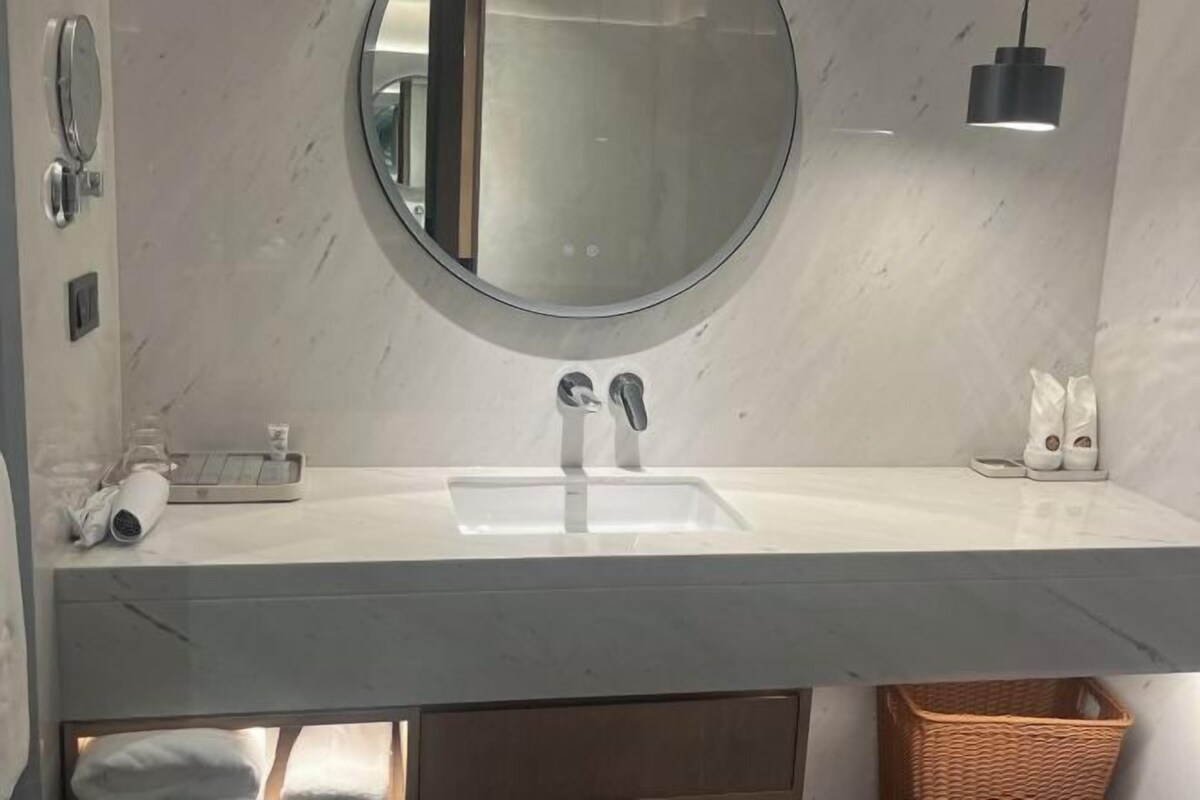 Een badkamer met een ronde spiegel, een wastafel, een handdoekhouder en een klein mandje.