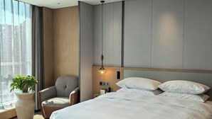 A modern hotel room with a large bed, a chair, a bedside table, a lamp, and a large window with curtains. - Jinhao International Hotel (Huaining)