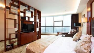 A hotel room with a large bed, a TV, a desk, and a view of the city.