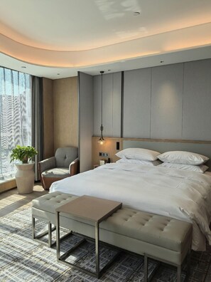 Una habitación de hotel moderna con una cama grande, una zona de estar, una planta en maceta y vistas por la ventana.