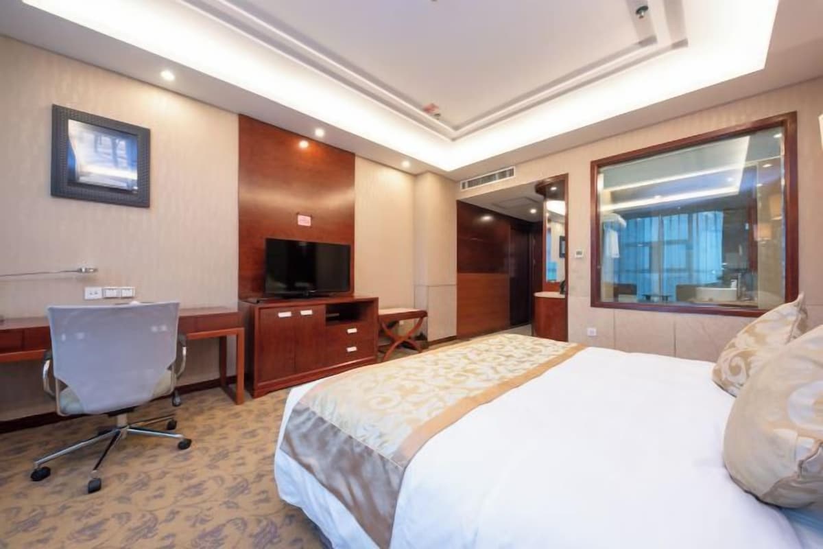 A hotel room with a bed, desk, television, and a bathroom visible through a glass door.