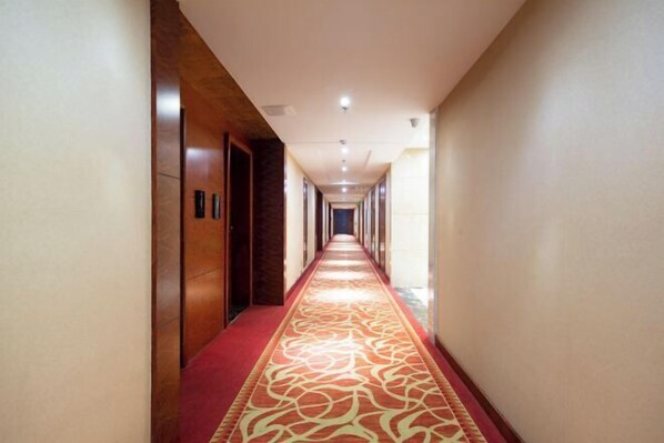 A long, narrow hotel corridor with a patterned carpet and wooden walls.