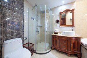 A bathroom with a glass-enclosed shower, a white toilet, a wooden vanity with a mirror, and a tiled wall.