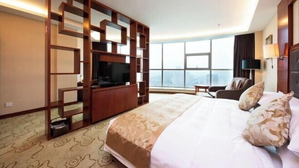 A hotel room with a large bed, a TV, a seating area, and a view of the city. - Jinhao International Hotel (Huaining)