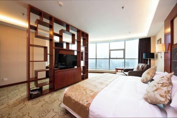 Ein Hotelzimmer mit einem großen Bett, einem Fernseher, einer Sitzecke und Blick auf die Stadt.