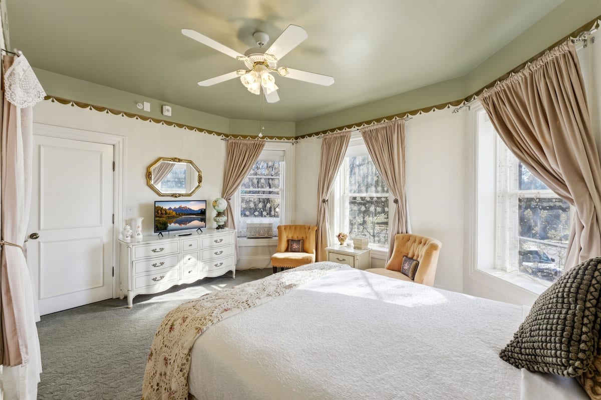 A bedroom with a bed, a chair, a dresser, a mirror, and a ceiling fan.