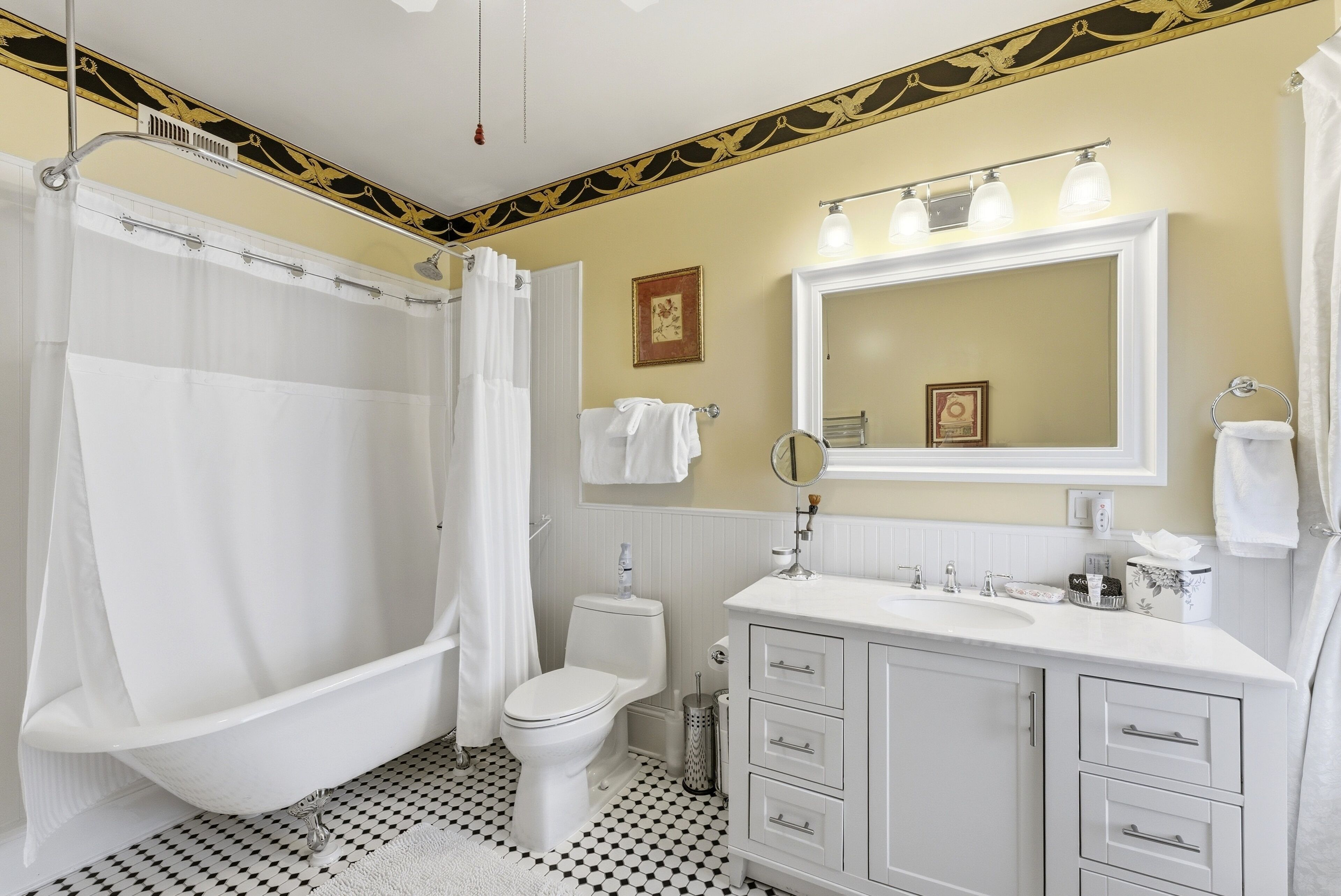 Un bany amb una banyera autònoma, un vàter, un lavabo amb calaixos, un mirall i una cortina de dutxa.